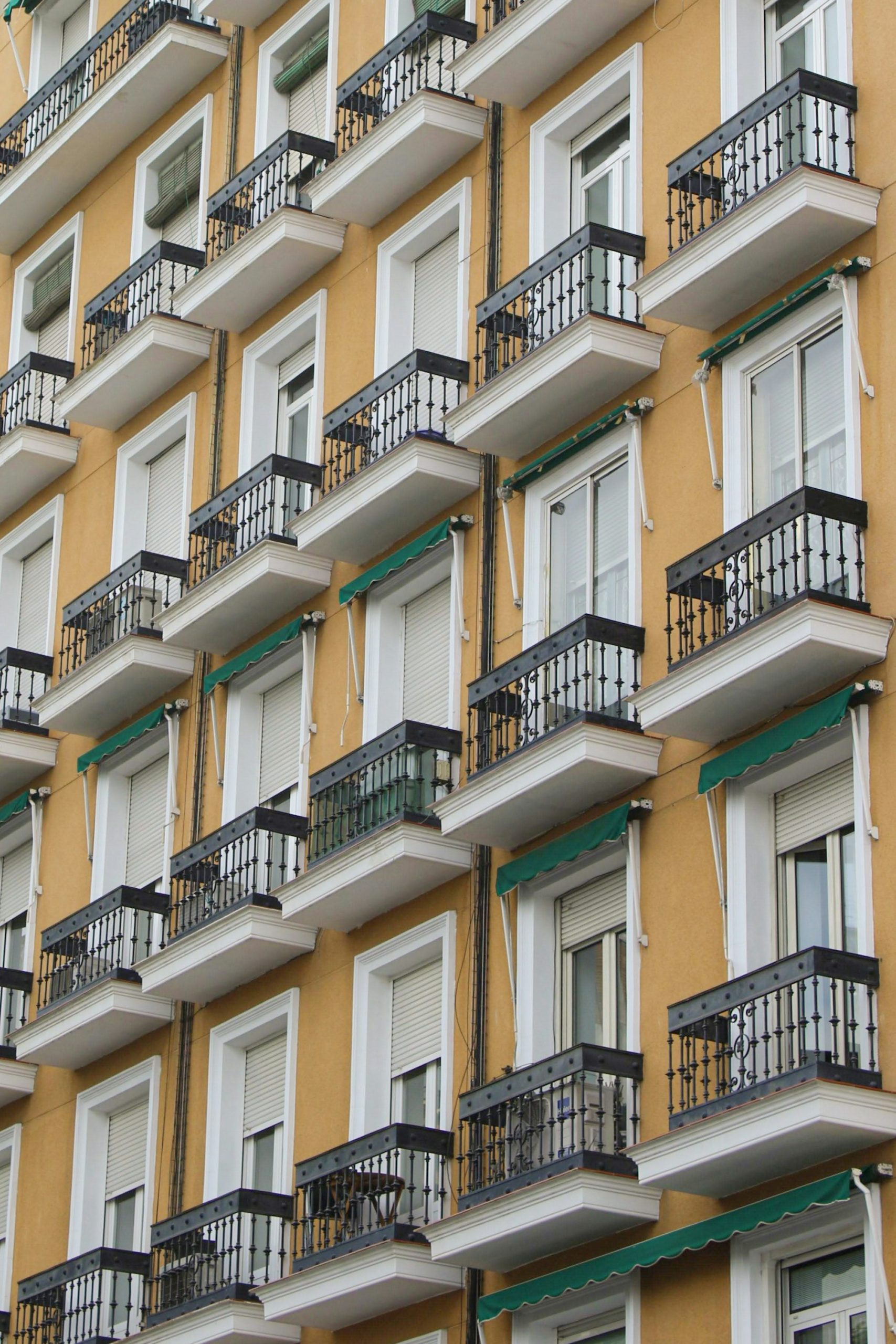 Fachada de un edificio de viviendas con balcones de forja repetidos y toldos verdes